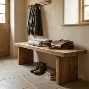 Puede incluir: Banco de madera r&uacute;stico con una manta, una cartera de cuero y botas. El banco es de madera en bruto y tiene un acabado natural. Un perchero con chaquetas cuelga sobre el banco. El suelo es de baldosas de piedra.