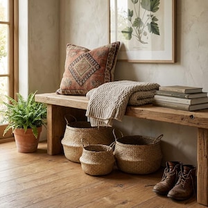 Puede incluir: Un interior acogedor con un banco de madera con un coj&iacute;n estampado y una manta beige doblada. Cestas tejidas de varios tama&ntilde;os est&aacute;n en el suelo. Un helecho en maceta y una impresi&oacute;n bot&aacute;nica completan la escena.