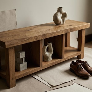 Puede incluir: Banco de madera con acabado natural, con una balda inferior y dos jarrones decorativos. Dos pares de zapatos de cuero marr&oacute;n est&aacute;n colocados en el suelo. El banco mide aproximadamente 122 cm de largo.