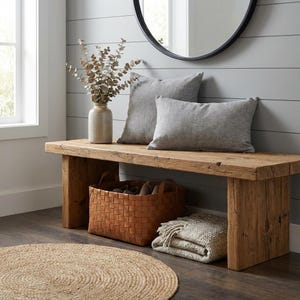 Puede incluir: Un banco de madera r&uacute;stica con dos cojines de lino gris, una cesta de cuero trenzado y una manta beige doblada. Una alfombra redonda de yute est&aacute; en el suelo. Un jarr&oacute;n con ramas secas y un espejo con marco negro.