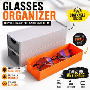 May include: A stackable glasses organizer set featuring two light gray rectangular storage units with pull-out drawers and one bright orange open tray. A pair of black-framed glasses rests inside the orange tray. Text includes GLASSES ORGANIZER.