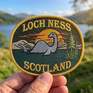 May include: An oval embroidered patch featuring a gray creature in dark green water, a yellow sun, brown mountains, and a green pine tree. The text LOCH NESS is embroidered in yellow at the top, and SCOTLAND is embroidered in yellow at the bottom.