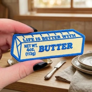 May include: Embroidered patch in the shape of a butter container, with the text "LIFE IS BETTER WITH BUTTER." The patch is light yellow with blue trim and text. It reads "NET WT. 4oz (113g)."