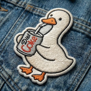 May include: Embroidered patch featuring a white goose drinking from a Diet Coke can. The goose has an orange beak and feet, with the words "Diet Coke" on the can. The patch is stitched with black, gray, orange, and red thread.
