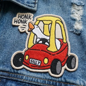 May include: Embroidered patch featuring a white goose driving a red and yellow toy car. The car has the word "SILLY" on the front. A speech bubble says "HONK HONK". The patch is on a denim jacket.