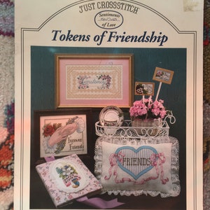 Op de afbeelding: Een boekje met borduurpatronen met de titel "Tokens of Friendship" uit de collectie "Sentiments of Love". Het boekje bevat vijf verschillende borduurpatronen, waaronder een hartvormig kussen met het woord "FRIENDS" erop geborduurd.