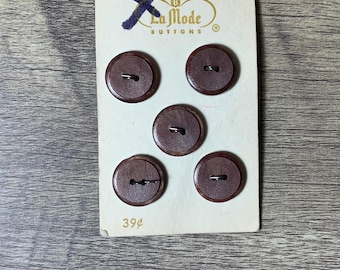 May include: A card of five brown wooden buttons with two holes each. The card is white with the text "La Mode Buttons" and "39¢" printed on it.