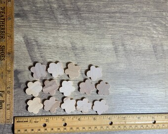 May include: A collection of 12 unfinished wooden flower shapes, each measuring approximately 2.5 cm in diameter. The shapes are arranged on a wooden surface.