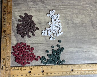 May include: Three piles of small, two-hole buttons in brown, red and green colours. The buttons are arranged on a wooden surface with a ruler.