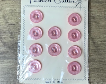 May include: A pack of ten pink plastic buttons with a white label that reads "UNUSUAL VALUE in Fashion Buttons" and "MADE IN JAPAN".