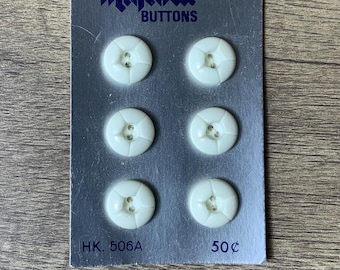May include: A card of six white plastic buttons with four holes each. The card is silver with blue text that reads "Majestic Buttons" and "HK. 506A 50¢".