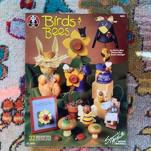 Könnte beinhalten: Ein Bastelbuch mit dem Titel "Birds & Bees" mit 32 bezaubernden Designs. Der Umschlag zeigt eine Auswahl an bemalten Holzhandwerken, darunter eine Biene, ein Vogel, eine Blume, ein Pilz und ein Honigtopf. Das Buch ist von Shirley Baer, Dianna Baer und Denise Basinger.