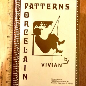 Puede incluir: Un libro marrón y blanco titulado "Patterns for Porcelain" de Vivian. La portada del libro presenta una silueta de una persona sentada en un columpio con un árbol en el fondo. El libro está encuadernado con una encuadernación en espiral.