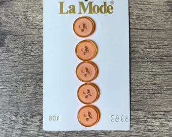 May include: A card of six peach-coloured plastic buttons with four holes each. The card has the text "La Mode" and the numbers "80¢" and "2808" printed on it.