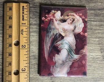 May include: A vintage-style magnet featuring a painting of an angel with wings, wearing a white gown and green sash, against a red background with floral accents.