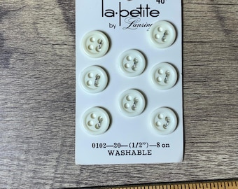 May include: A card of eight white plastic buttons with four holes each. The buttons are 1/2 inch in diameter and are washable. The card reads "la-betite by Lansing" and "0102-20-(1/2")-8 on WASHABLE".