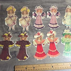 Puede incluir: Un conjunto de 10 muñecas de papel, con niñas que llevan diferentes vestidos y sombreros. Las muñecas están impresas en cartulina y están listas para ser recortadas y jugadas. Las muñecas están todas vestidas con diferentes colores y estilos, incluyendo rosa, azul, verde, rojo y amarillo.