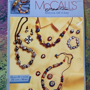 Pode incluir: Um kit de artesanato McCall's Creates Slices of Clay com um fundo amarelo e uma variedade de contas, botões e brincos de argila coloridos. O kit inclui instruções para fazer joias e outros artesanatos.