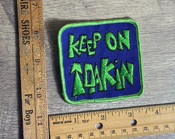 May include: Green and blue embroidered patch with the text "Keep on Tokin'" in a stylised font.
