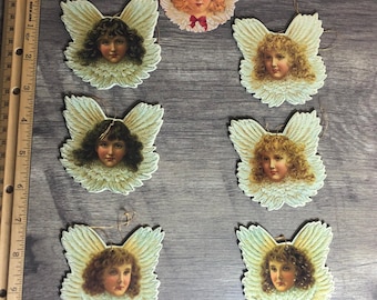 May include: Eight vintage angel ornaments with white wings and gold trim. Each angel has a different facial expression and hairstyle. The angels are made of paper and have a hole at the top for hanging.