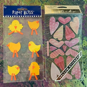 May include: Two sheets of stickers. One sheet has yellow chicks with orange beaks and feet. The other sheet has pink and white hearts with a variety of patterns. The text on the sheet of hearts reads "Vellum Stickers".