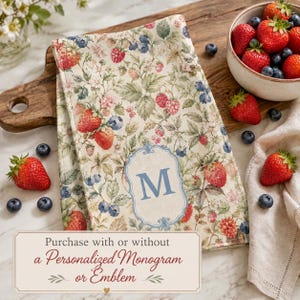 May include: A kitchen towel featuring a botanical print of strawberries, raspberries, and blueberries on a cream background, with a central light blue decorative frame containing the letter M. The text reads: Purchase with or without a Personalized Monogram or Emblem.