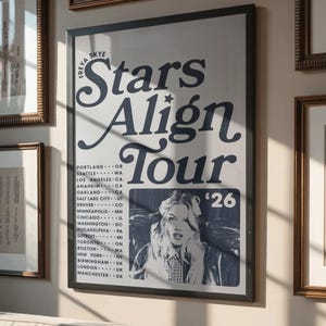 Puede incluir: Un póster enmarcado con el texto "Freya Skye Stars Align Tour" en una fuente decorativa. El póster incluye una imagen en blanco y negro de una mujer y una lista de ciudades de la gira. El póster se exhibe en una pared con otras obras de arte enmarcadas.