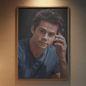 May include: A framed portrait of a man in a blue shirt, hanging above a beige sofa. The room is dimly lit with a lamp on a side table and a wooden coffee table in front of the sofa. The wall has a textured pattern.