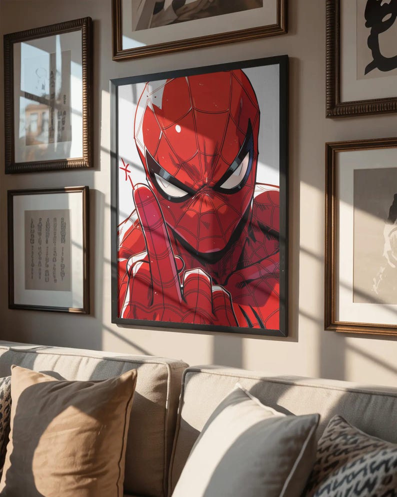 May include: Framed artwork featuring a close-up of Spider-Man in his red and black suit, giving a hand gesture. The artwork is in a black frame and hangs on a wall with other framed pieces. The image is set above a beige sofa.