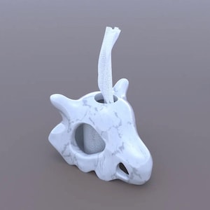 May include: A white marble-effect bath sponge in the shape of a skull, with a white hanging loop. The skull features eye and mouth openings, and a hole at the top for the loop. The sponge is a light grey colour.