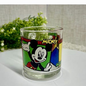 Peut inclure: Verre transparent avec un motif de Mickey Mouse. Le verre pr&eacute;sente une image de Mickey Mouse, avec le mot "MICKEY". Le verre est de forme cylindrique et convient aux boissons. Hauteur du verre : environ 9 cm.