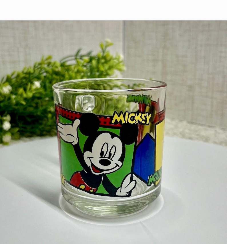 Peut inclure: Verre transparent avec un motif de Mickey Mouse. Le verre pr&eacute;sente une image de Mickey Mouse, avec le mot "MICKEY". Le verre est de forme cylindrique et convient aux boissons. Hauteur du verre : environ 9 cm.