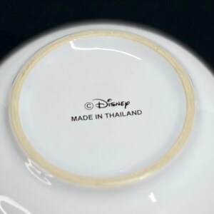 K&ouml;nnte beinhalten: Wei&szlig;er Keramiknapf mit hellem beigen Rand. Der Napf hat das Disney-Logo und den Text "MADE IN THAILAND" auf der Unterseite aufgedruckt.