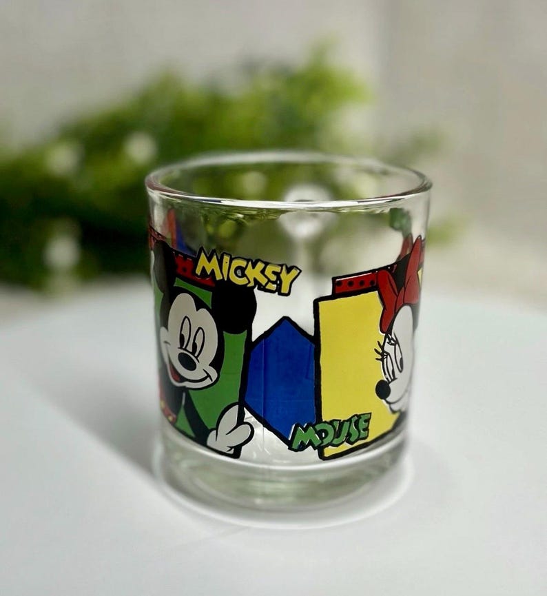 Peut inclure: Verre transparent avec Mickey et Minnie Mouse. Le verre pr&eacute;sente un design color&eacute; avec les mots "Mickey Mouse". Le design comprend des accents verts, jaunes, bleus et rouges. Un ajout amusant &agrave; la collection de tout fan de Disney.