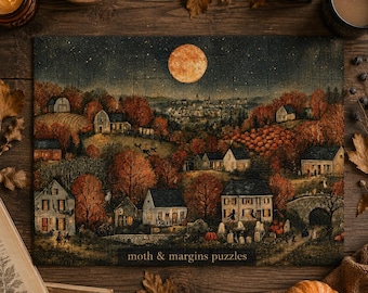 Può includere: Un puzzle rettangolare che raffigura un paesaggio autunnale notturno con una grande luna arancione, case sparse e alberi dal fogliame arancione. Il testo "moth & margins puzzles" è stampato in piccolo nella parte inferiore centrale.