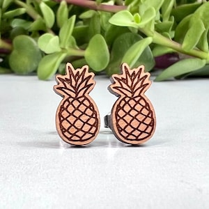 May include: A pair of wooden pineapple earrings. The earrings are brown and have a detailed pineapple design.