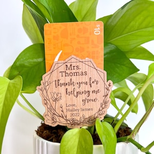 May include: A wooden plant tag with the text "Mrs. Thomas Thank you for helping me grow. Love, Hailey James 2022" is attached to a potted plant.