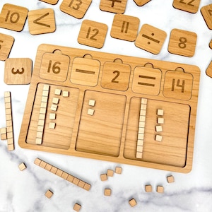May include: Wooden math learning set with a light brown finish. The set includes a wooden tray with slots, number tiles, and wooden blocks for counting and basic arithmetic. Numbers and symbols are engraved on the wooden pieces.