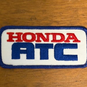 May include: Rectangular patch with the word "HONDA" in red block letters above "ATC" in blue block letters. The patch has a white background with a blue border.