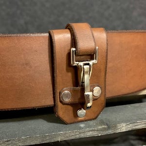 May include: A brown leather belt with a metal buckle and a leather loop for attaching keys or other items.
