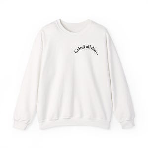 May include: White crew neck sweatshirt with the text "Grind all day..." in a curved, dark navy font. The sweatshirt has long sleeves and a relaxed fit, suitable for casual wear.