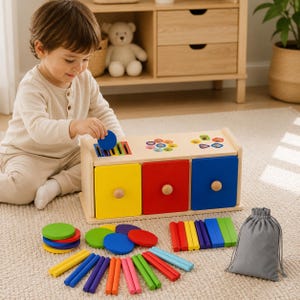 May include: A wooden sorting toy with three colorful drawers in yellow, red, and blue. The top features slots and holes for inserting various wooden shapes, including circles and rectangular bars in multiple colors, alongside a gray drawstring bag.