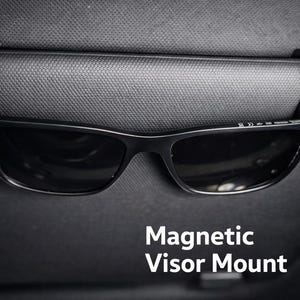May include: A black magnetic visor mount holding a pair of black sunglasses. The mount is attached to a car visor. The text "Magnetic Visor Mount" is displayed in white.