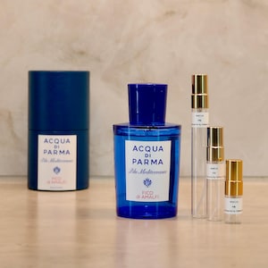 Può includere: Un flacone di profumo cilindrico blu con un'etichetta bianca che riporta la scritta Acqua di Parma Blu Mediterraneo Fico di Amalfi, un contenitore blu abbinato e tre flaconcini campione in vetro trasparente con tappi dorati.