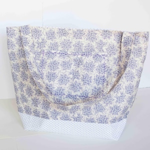 Op de afbeelding: Een draagtas met een blauw en crèmekleurig bloemmotief. Het heeft een voorvak en een stippenpatroon aan de onderkant. De handvatten zijn gemaakt van dezelfde bloemenstof. Een praktische en stijlvolle accessoire.
