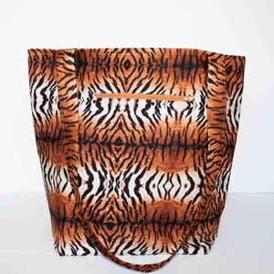 May include: A large tote bag with a tiger stripe pattern in shades of brown, black, and white. The bag has a zippered pocket and matching handles. The bag is made of a sturdy fabric.