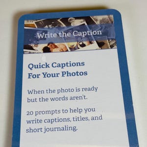 May include: A rectangular card with a blue border featuring the text Write the Caption, Quick Captions For Your Photos, When the photo is ready but the words aren't, 20 prompts to help you write captions, titles, and short journaling, and getTheo.com.