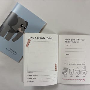 May include: A light blue activity book featuring a gray elephant illustration on the cover with the text Me By Me My Favorite Things. The open pages include prompts like My Favorite Drink, I drink it with, and What goes with your favorite drink?