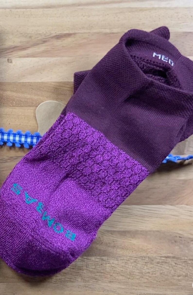 May include: A purple sock with a textured toe and heel, and the word "MED" printed on the cuff. The sock has a darker purple cuff and a lighter purple toe and heel. The brand name is printed in teal on the toe.