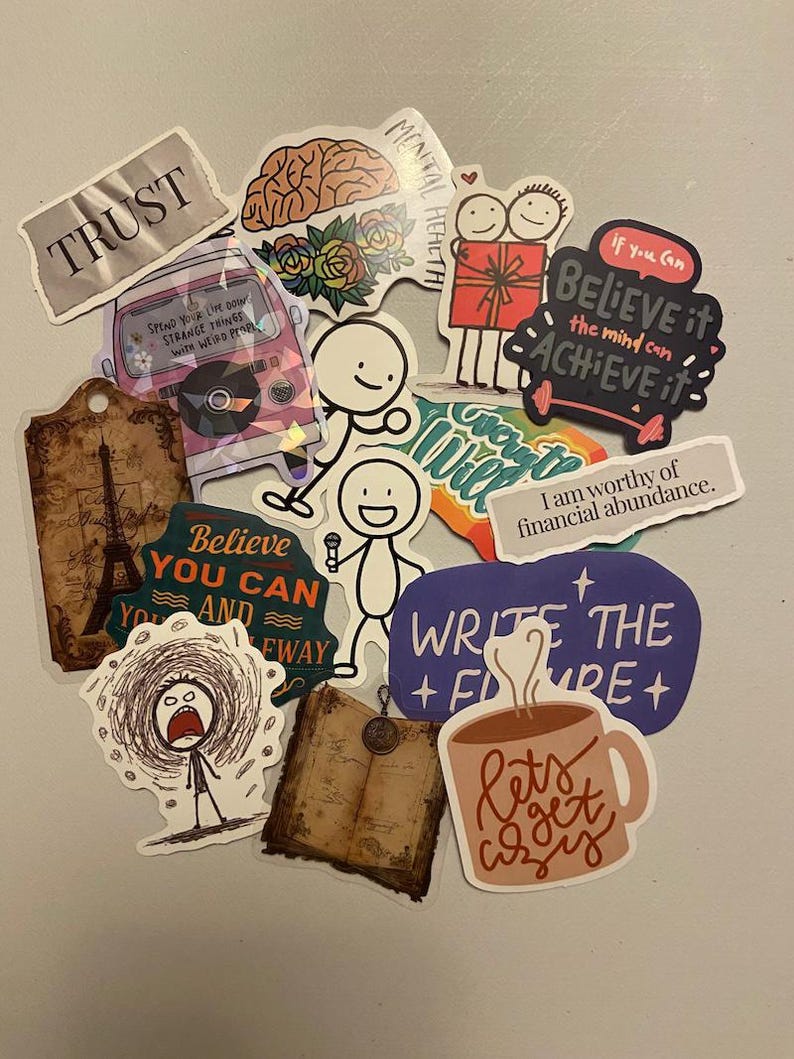 May include: A collection of colorful stickers with various designs and text. Stickers include phrases like "TRUST", "Believe you can", and "Let's get cozy". Other stickers feature illustrations of a brain, a coffee mug, and stick figures.